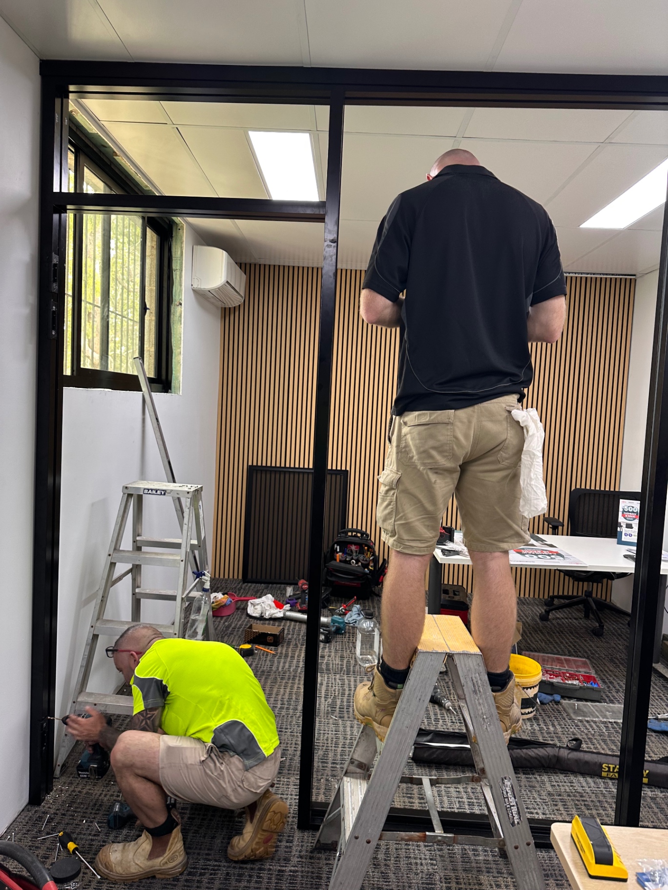 Two tradespeople fitting a black-framed glazed doorway during an interior project